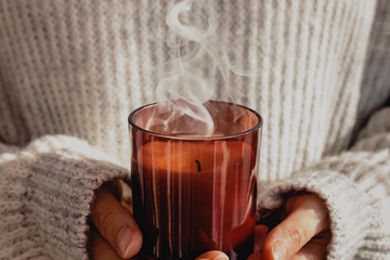 Softly scented amber candle on a neutral background, representing gentle candle scents for people with sensitive noses.