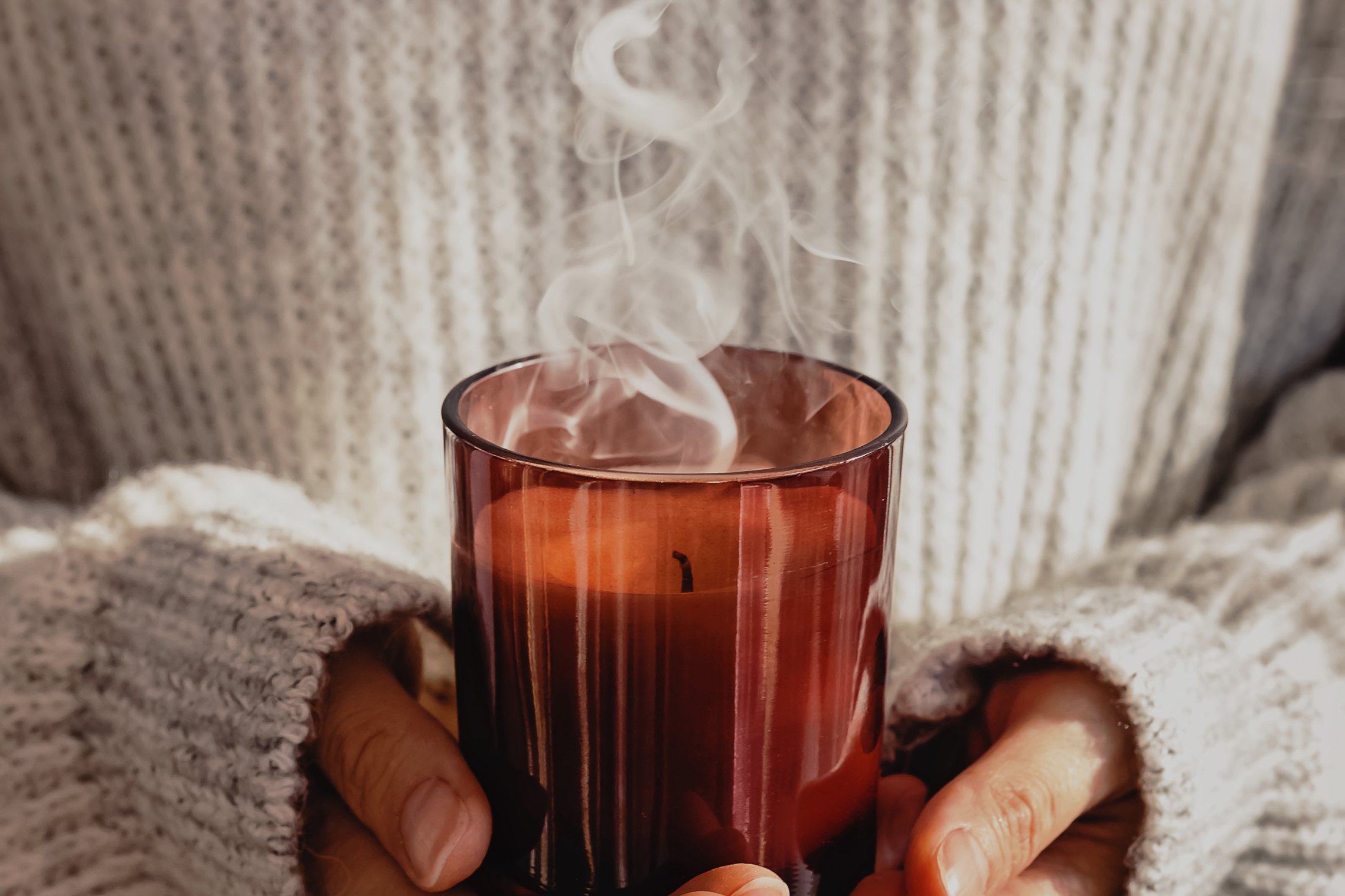 Softly scented amber candle on a neutral background, representing gentle candle scents for people with sensitive noses.