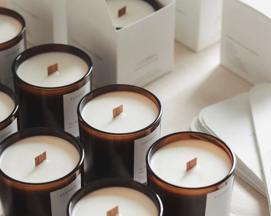 Close up of Luceria candles with wooden wick and gentle flame on warm-toned surface.
