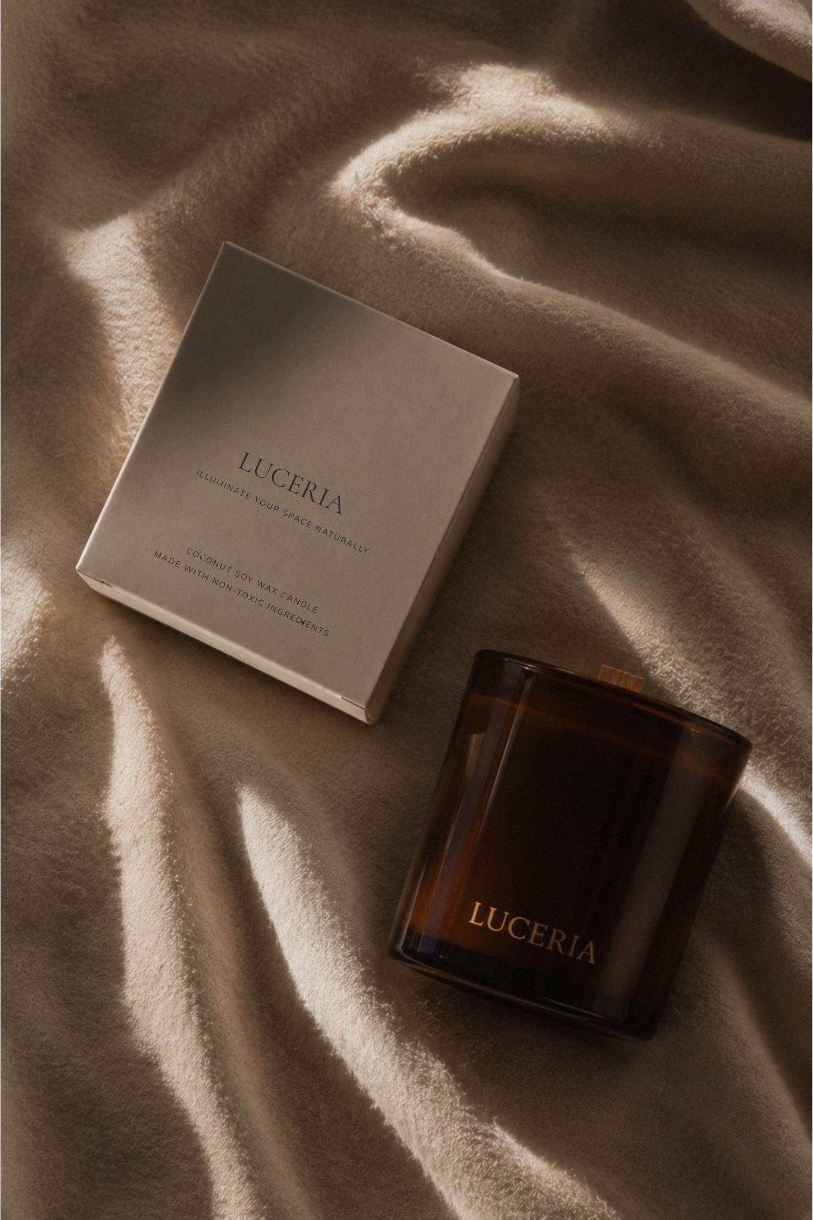 Luceria candle in an amber glass jar beside its luxury gift box, styled on soft draped fabric with warm natural light