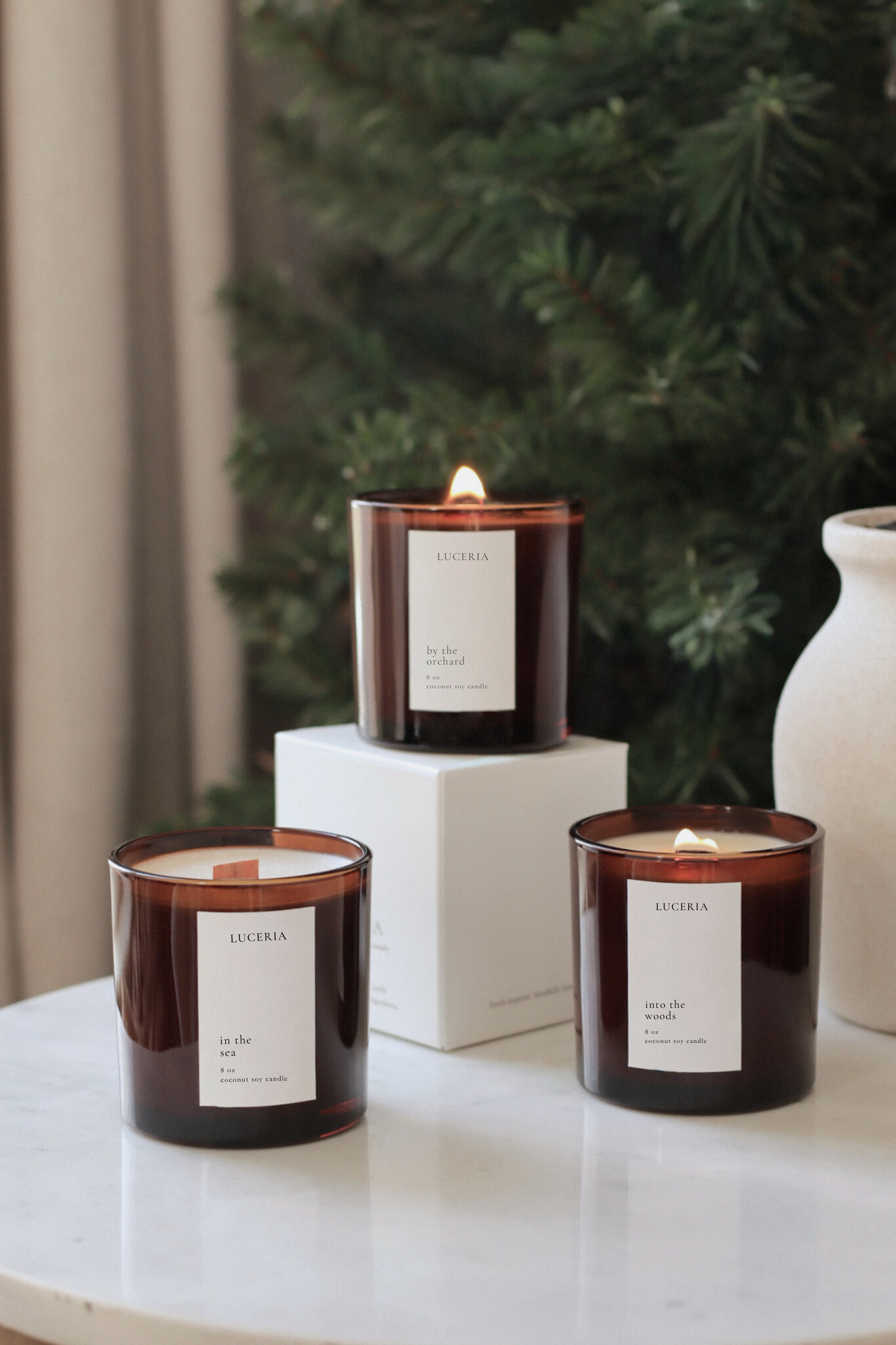 Three Earthen Collection Candles in brown amber colored glass jars on marble table with greenery and textured vase by Luceria Candle Co.