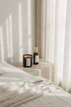 Luceria candle and bottle on a nightstand with soft light filtering through sheer curtains.