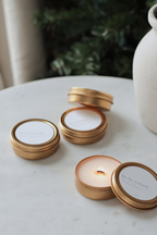 small gold tin candles on marble with greenery and textured vase.