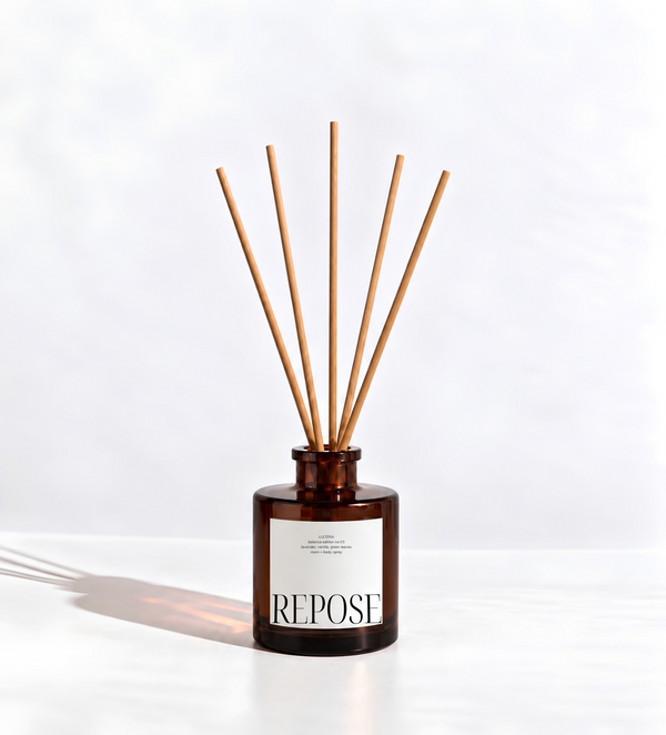 A Luceria reed diffuser bottle made of dark amber glass with a white label reading 'REPOSE' and natural wood reed sticks, set against a clean white background.