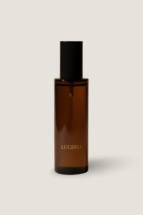 An amber glass bottle with a black cap and gold 'LUCERIA' branding, centered on a light beige background.