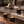 Three black wax candles in matte black jars with gold 'LUCERIA' branding, arranged on a wooden table with stacked books and a small vase in a cozy indoor setting.