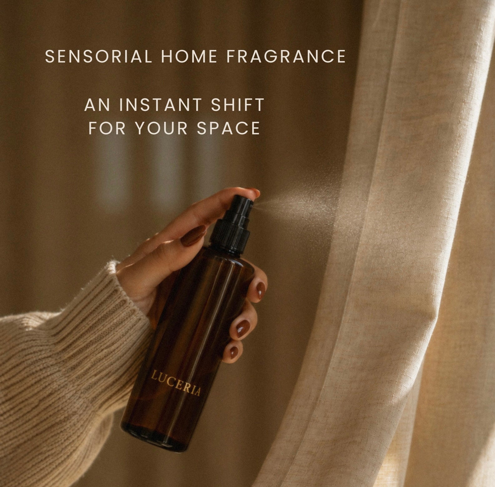 A hand in a cream ribbed sweater holds a dark amber spray bottle labeled LUCERIA, spraying a fine mist toward beige curtains. Text at the top reads, 'SENSORIAL HOME FRAGRANCE' and 'AN INSTANT SHIFT FOR YOUR SPACE'.