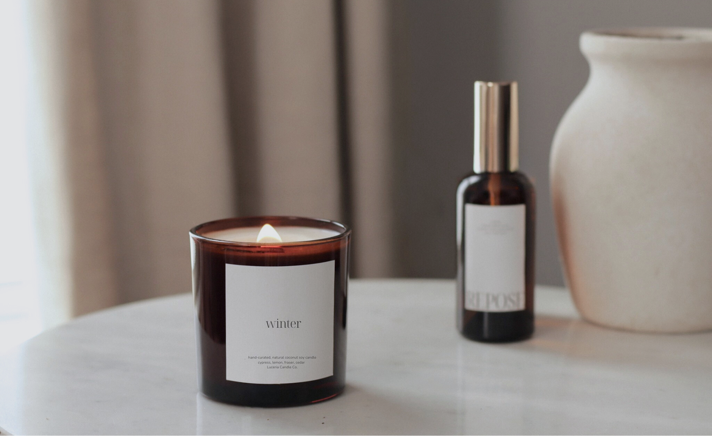 Luceria candle labeled 'winter' and a bottle of room spray on a marble table with a neutral background
