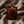 An amber glass candle jar with the brand name LUCERIA printed in gold near the bottom, lit with a small flame. The candle is set against a background of draped beige fabric.