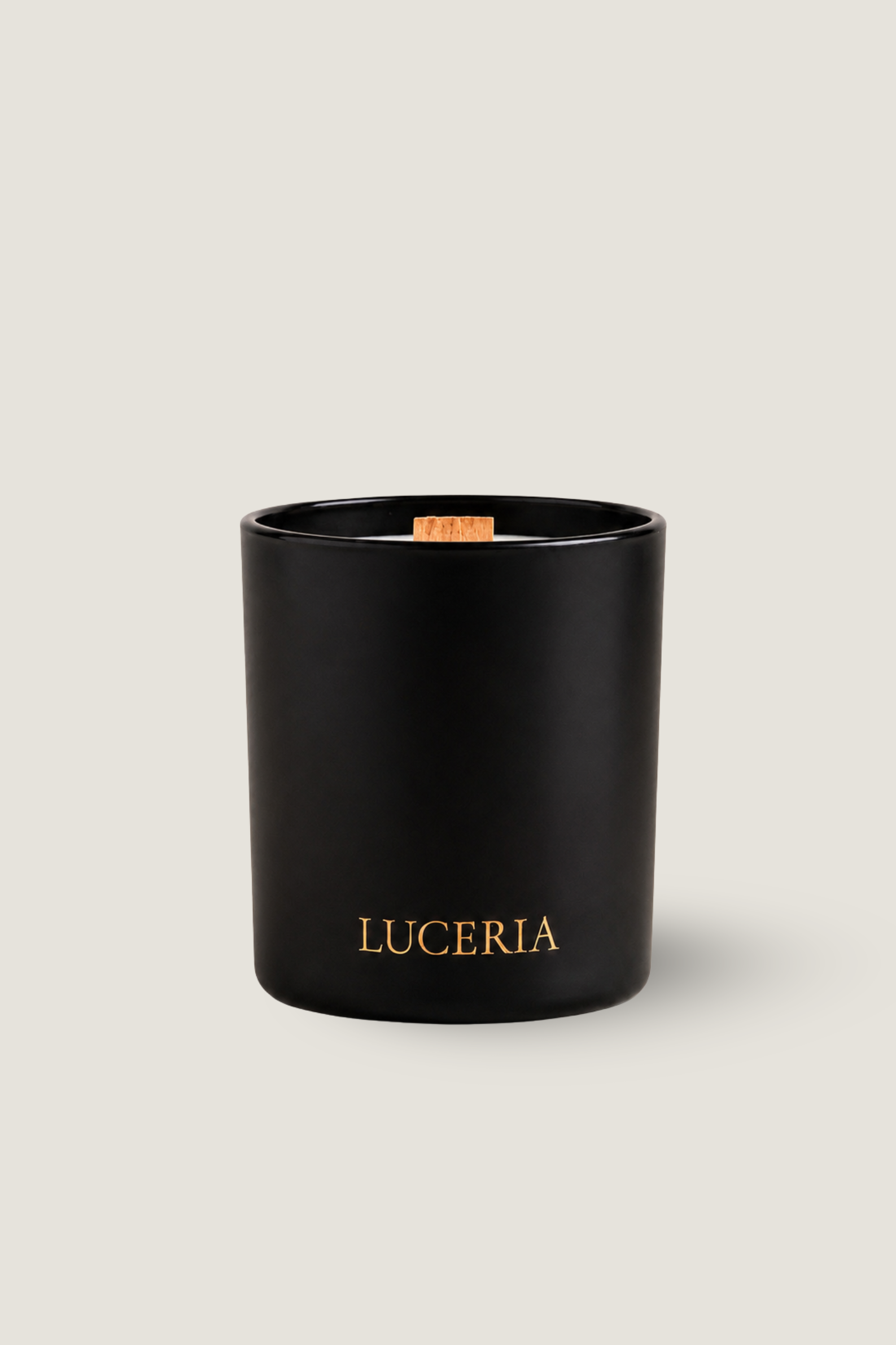 A matte black candle jar with gold 'LUCERIA' branding on the front, set against a solid light beige background.