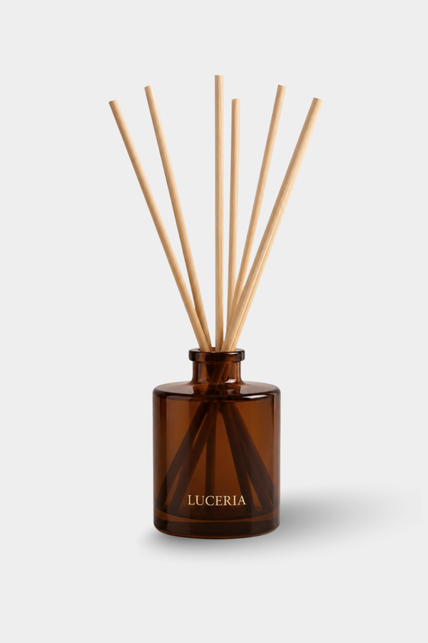 Amber glass reed diffuser bottle with natural wood diffuser sticks, labeled LUCERIA, on a light gray background.