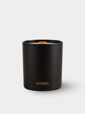 A matte black glass jar candle with a small wooden wick and gold 'LUCERIA' branding on the front, set against a light gray background.