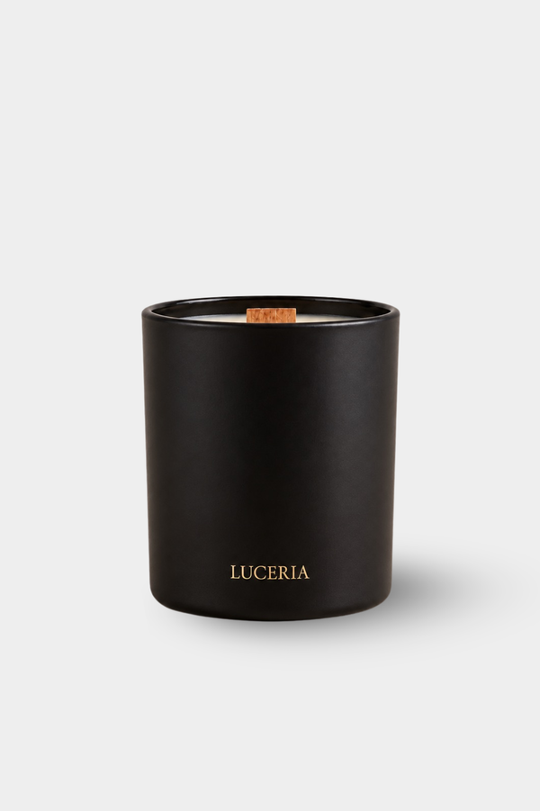 A matte black glass jar candle with a small wooden wick and gold 'LUCERIA' branding on the front, set against a light gray background.