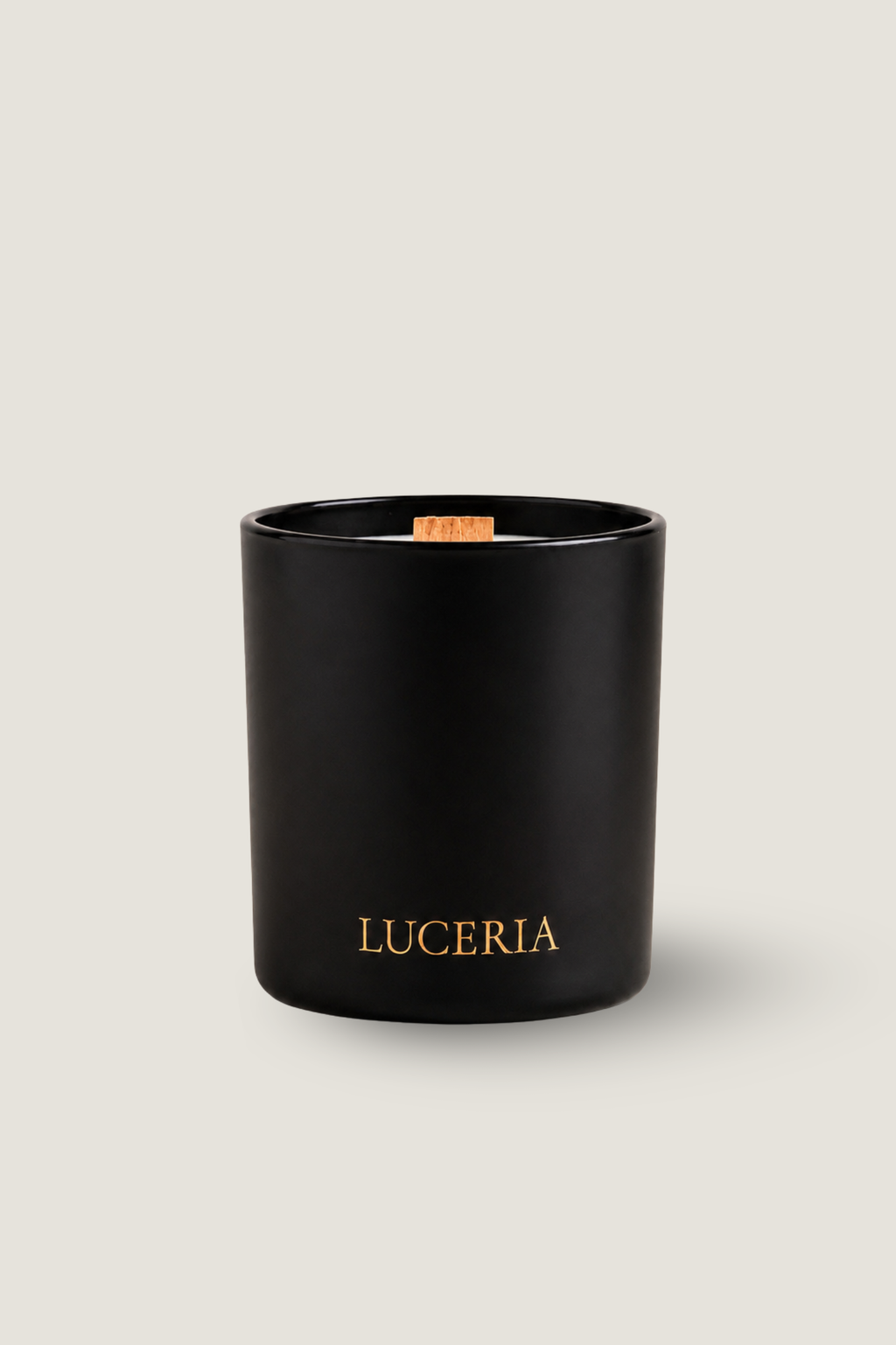 A matte black glass candle jar with gold 'LUCERIA' branding on the front, featuring a natural wood wick, set against a solid light beige background.