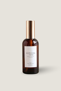 A bottle of Luceria Redwoods & Moss room spray with an amber brown glass body, a gold cap, and a white label, centered on a light beige background.