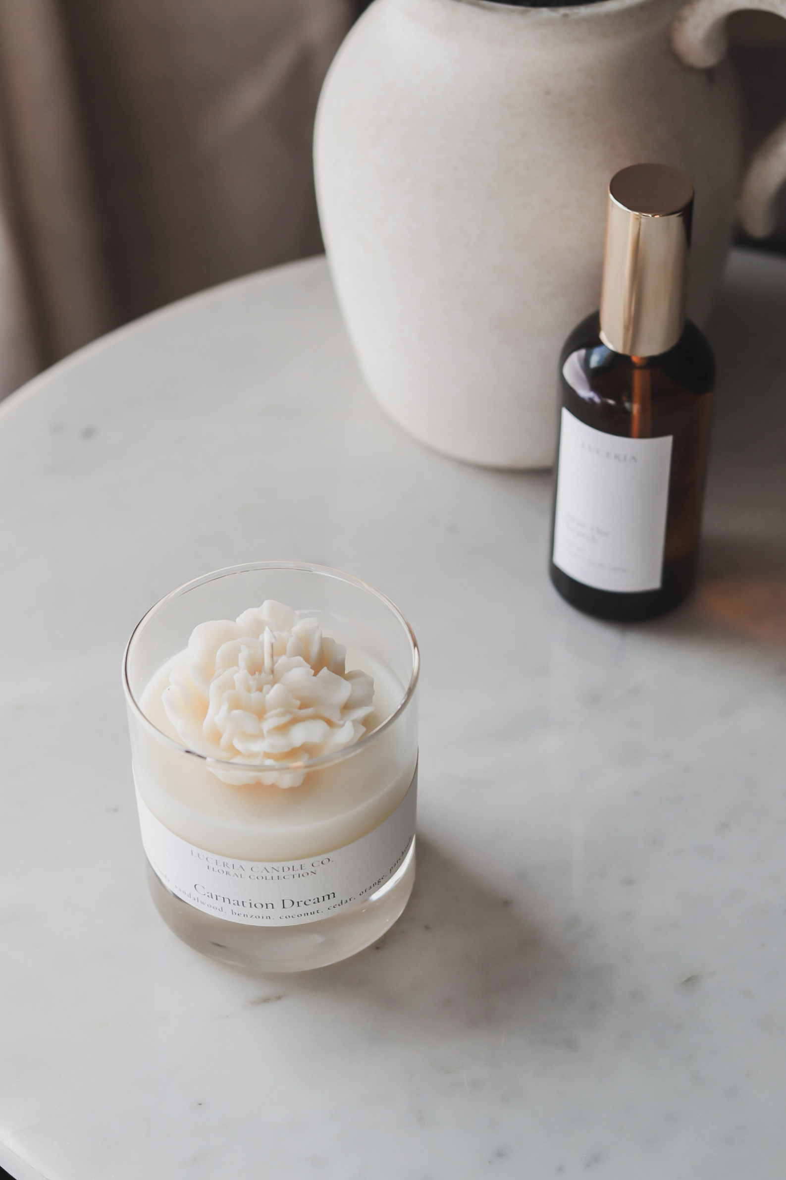 Glass jar with flower candle and bottle on a marble surface