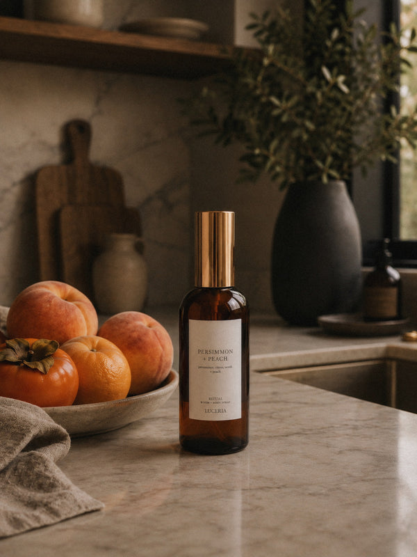 Luceria Persimmon and Peach room spray in an amber glass bottle styled with fresh persimmons, peaches, citrus and warm neutral home décor.