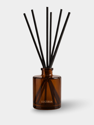 Amber glass reed diffuser bottle with black reeds and the brand name LUCERIA printed in gold on the front, set against a light gray background.