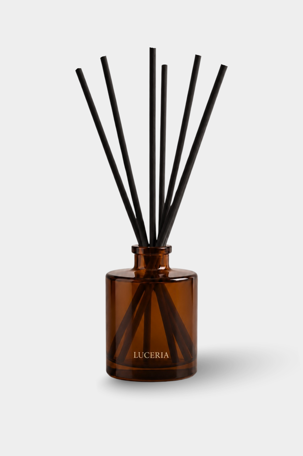 Amber glass reed diffuser bottle with black reeds and the brand name LUCERIA printed in gold on the front, set against a light gray background.