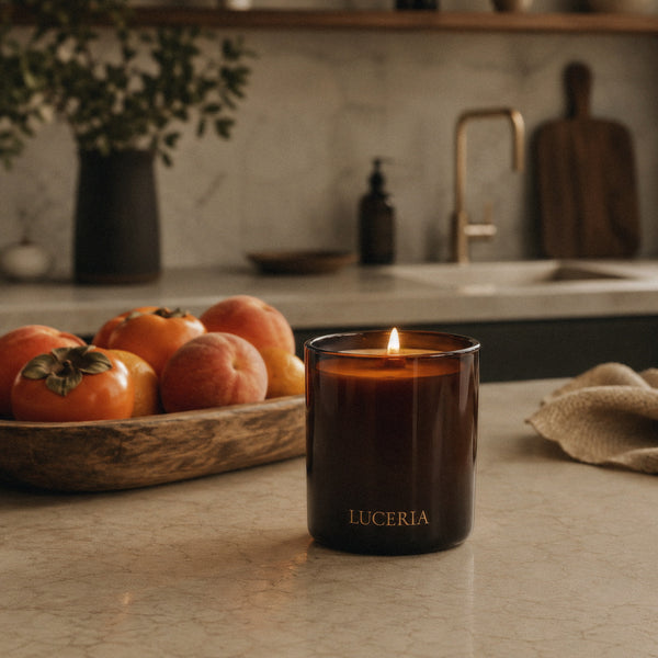 Luceria Persimmon and Peach candle with a natural wood wick styled beside fresh persimmons, peaches and warm neutral home décor.