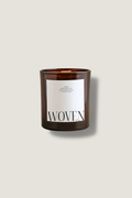 Candle with a label reading 'Woven' on a beige background