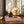 Amber glass Luceria reed diffuser bottle with wooden reeds, styled on stacked books on a wooden table with a mirror and warm window light in the background.