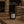A black matte candle in a dark glass jar sits on a stone surface in a cozy living room setting, with overlaid text detailing product features and scent name Autumn Woods by Luceria Candle Co.