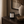 A black glass candle jar with a white label reading 'AUTUMN WOODS' by Luceria Candle Co. sits on a dark wooden console table in a styled interior setting with a ceramic vase and bowl nearby.
