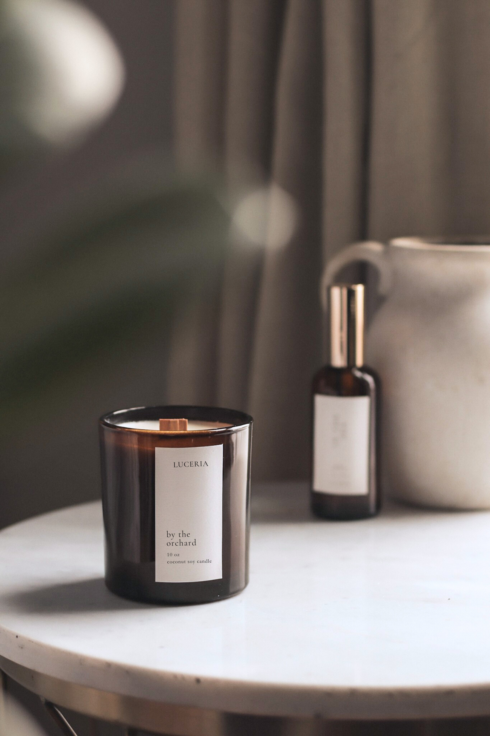 Persimmon citron scented candle and spray bottle on a table with a blurred background