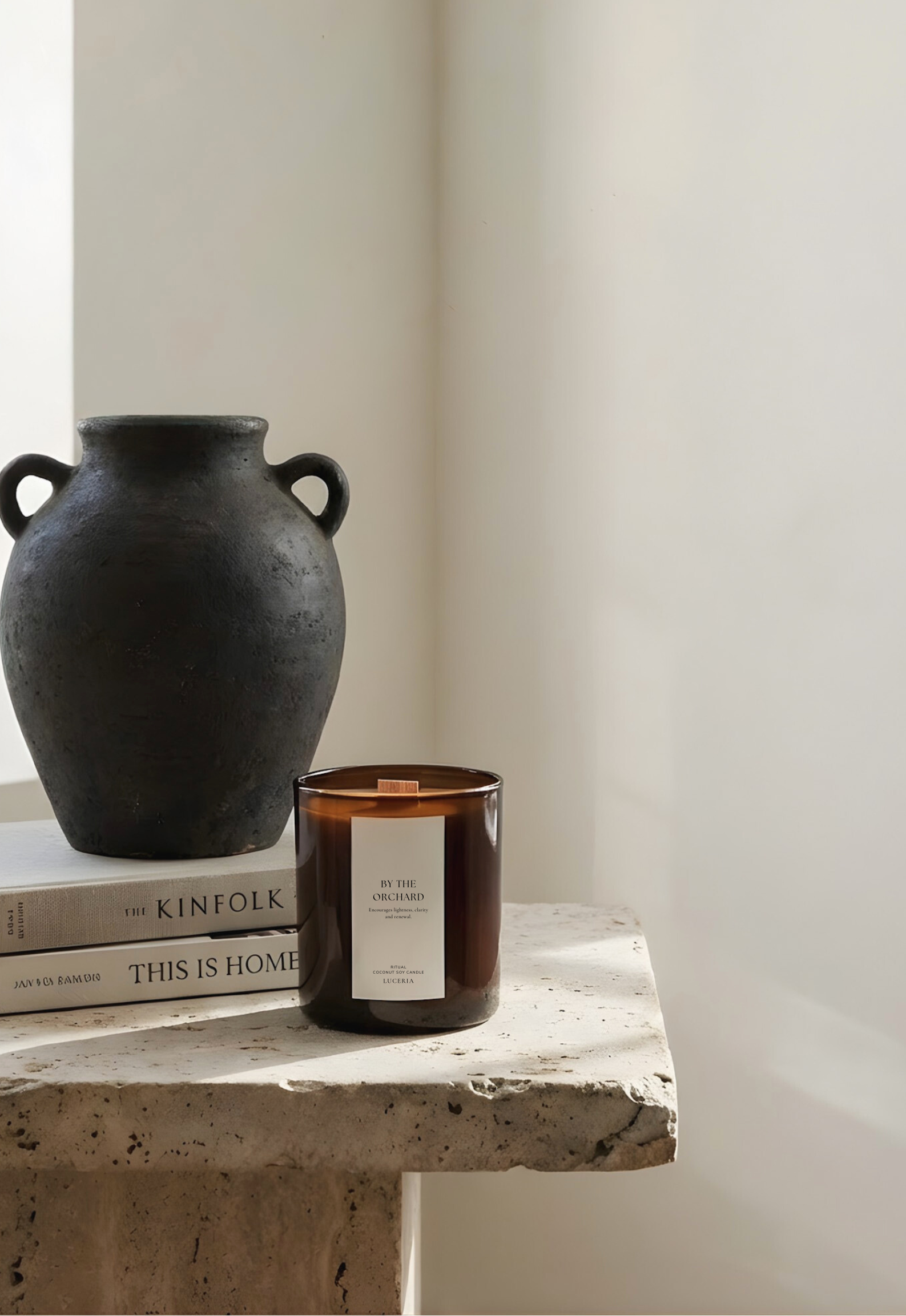 Black vase, books, and candle on a stone surface with a white wall background