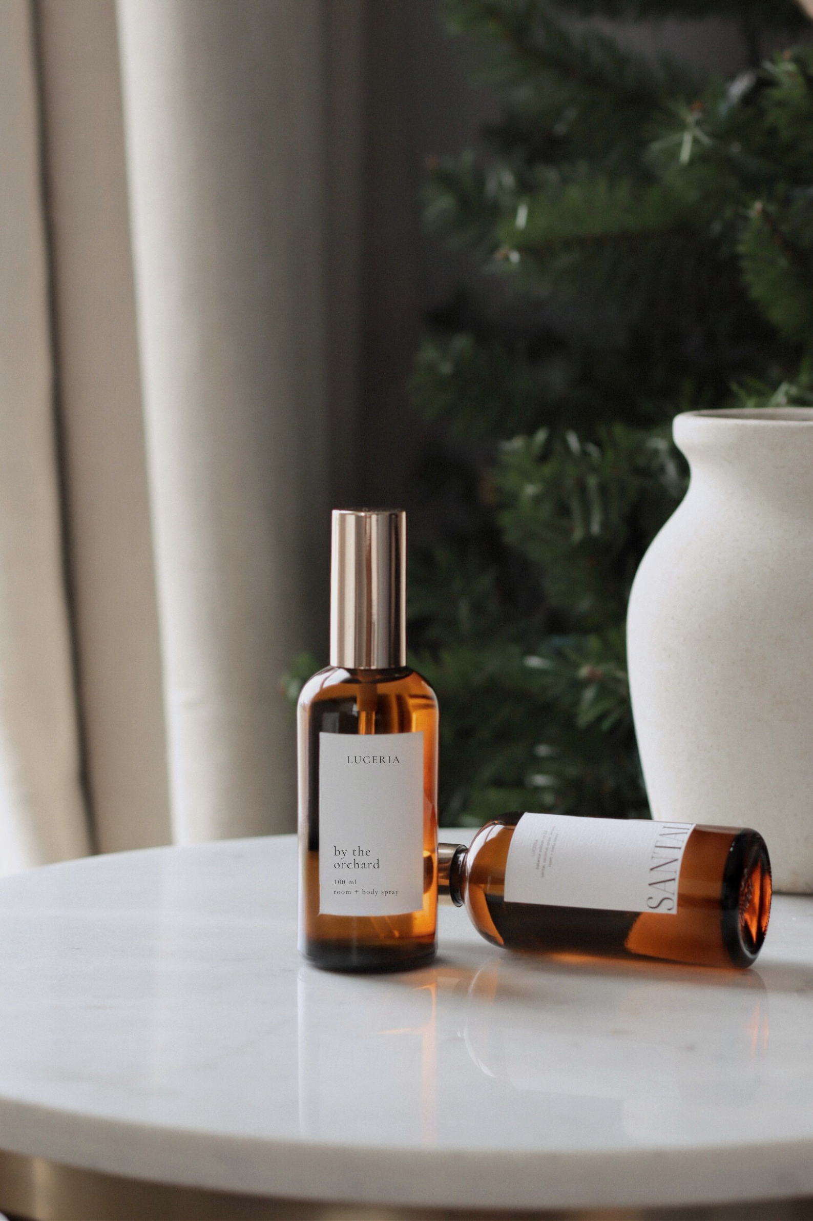 Two bottles of a product with visible labels on a marble surface, with a blurred green plant and white vase in the background.
