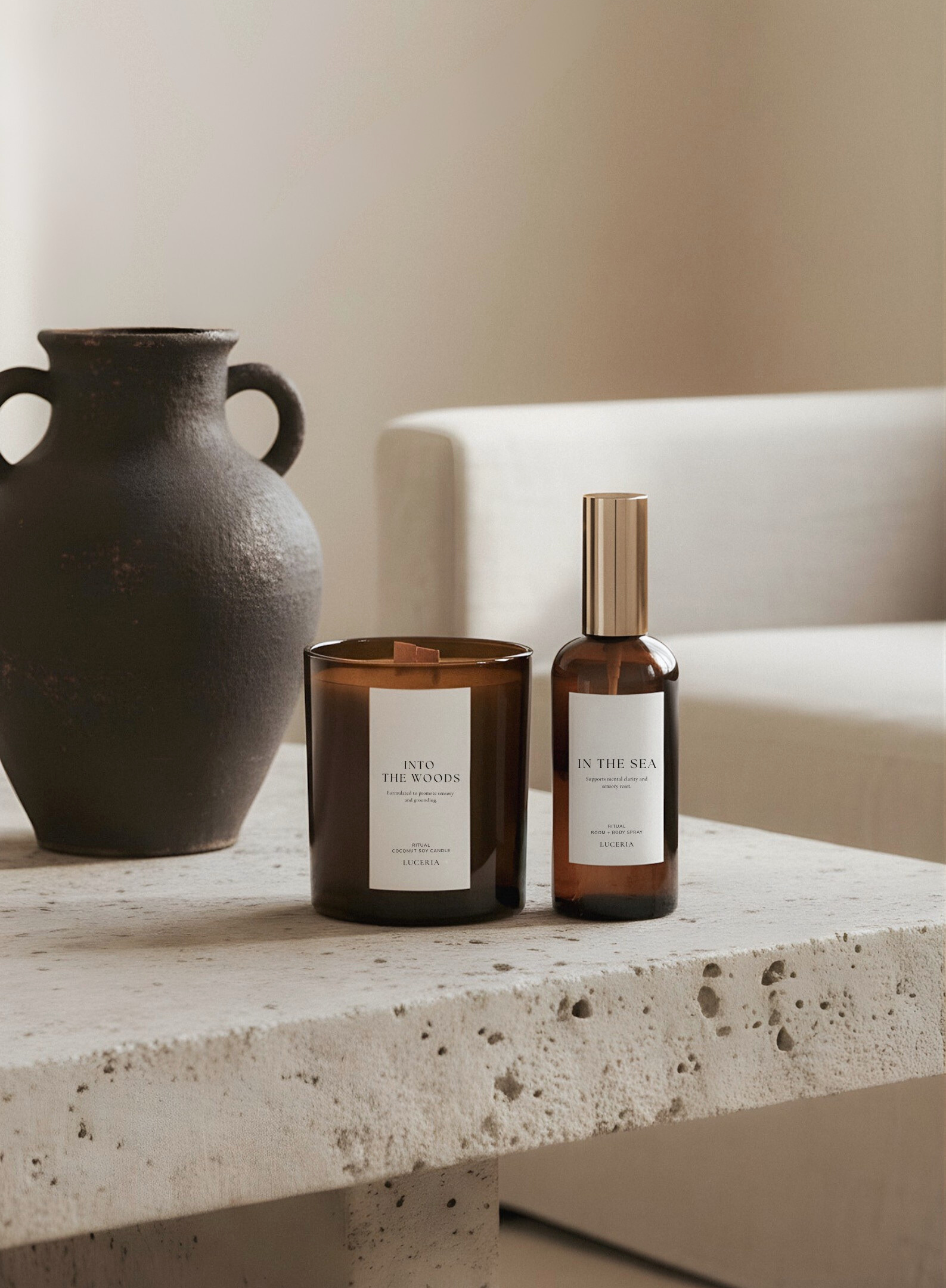 Candle and bottle on a stone table with a vase and branches in the background