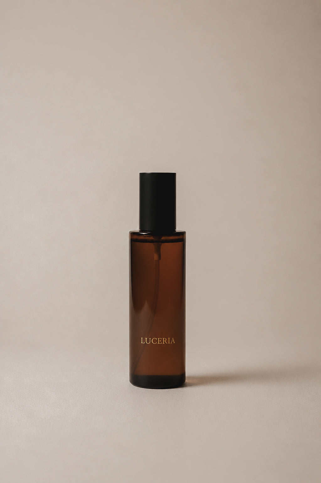 Luceria amber glass room and linen spray bottle with black cap and black nozzle on a neutral beige backdrop with soft diffused light. Bottle is labeled ‘LUCERIA’ with gold lettering.