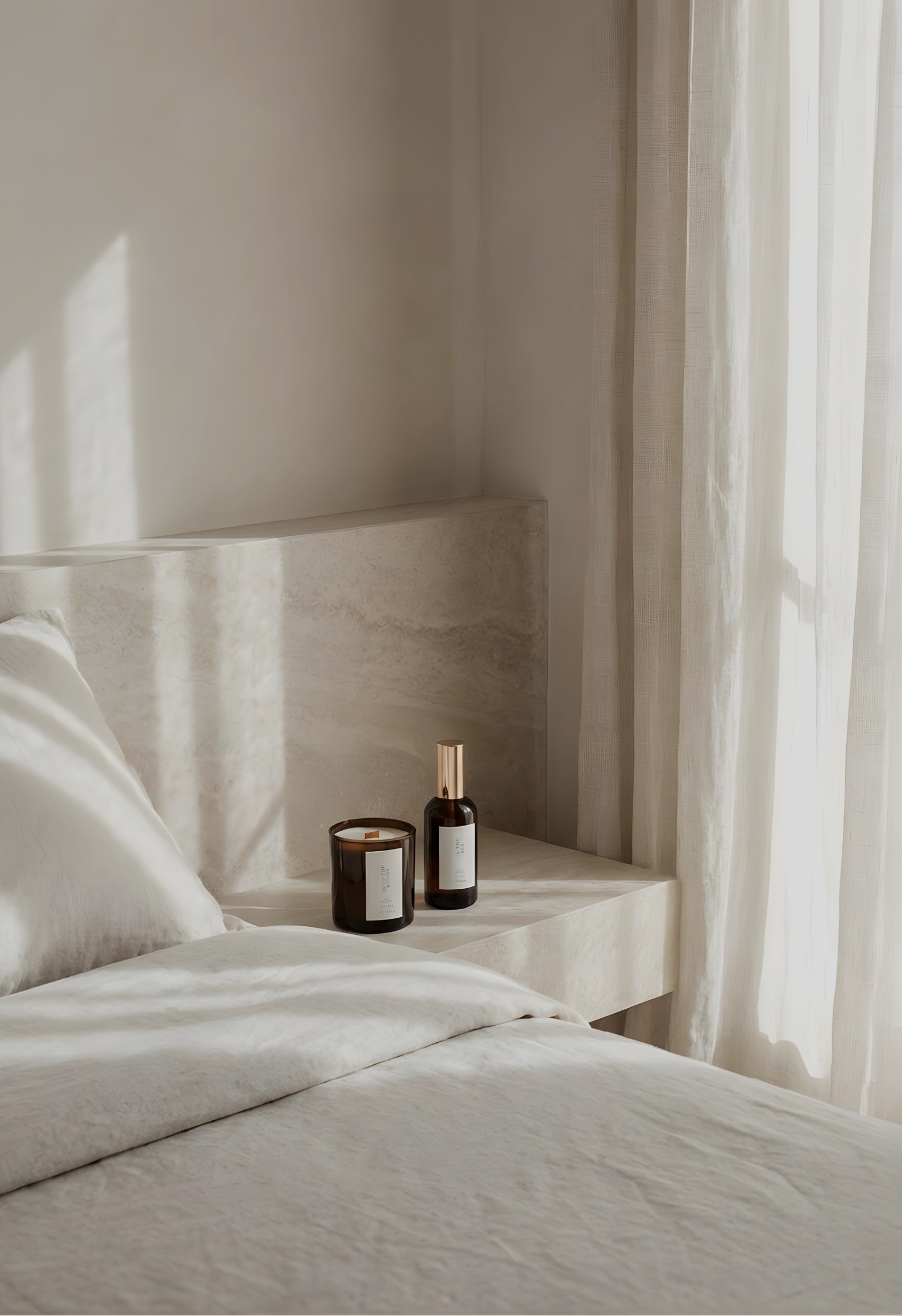 Neatly made bed with a nightstand holding two bottles and a candle, with light filtering through curtains.