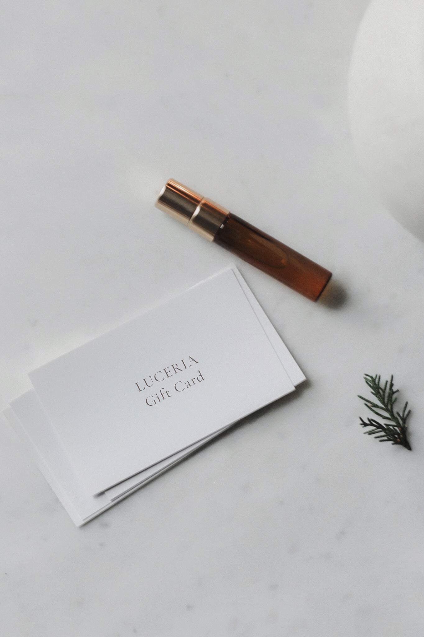 Amber rollerball bottle and white cards with 'LUCERIA' branding on a marble surface.