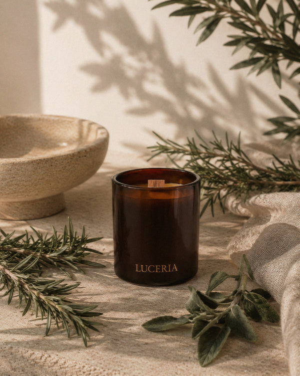 Luceria Rosemary and Sage candle with a natural wood wick styled beside fresh rosemary, sage leaves, pine sprigs, and neutral home décor.