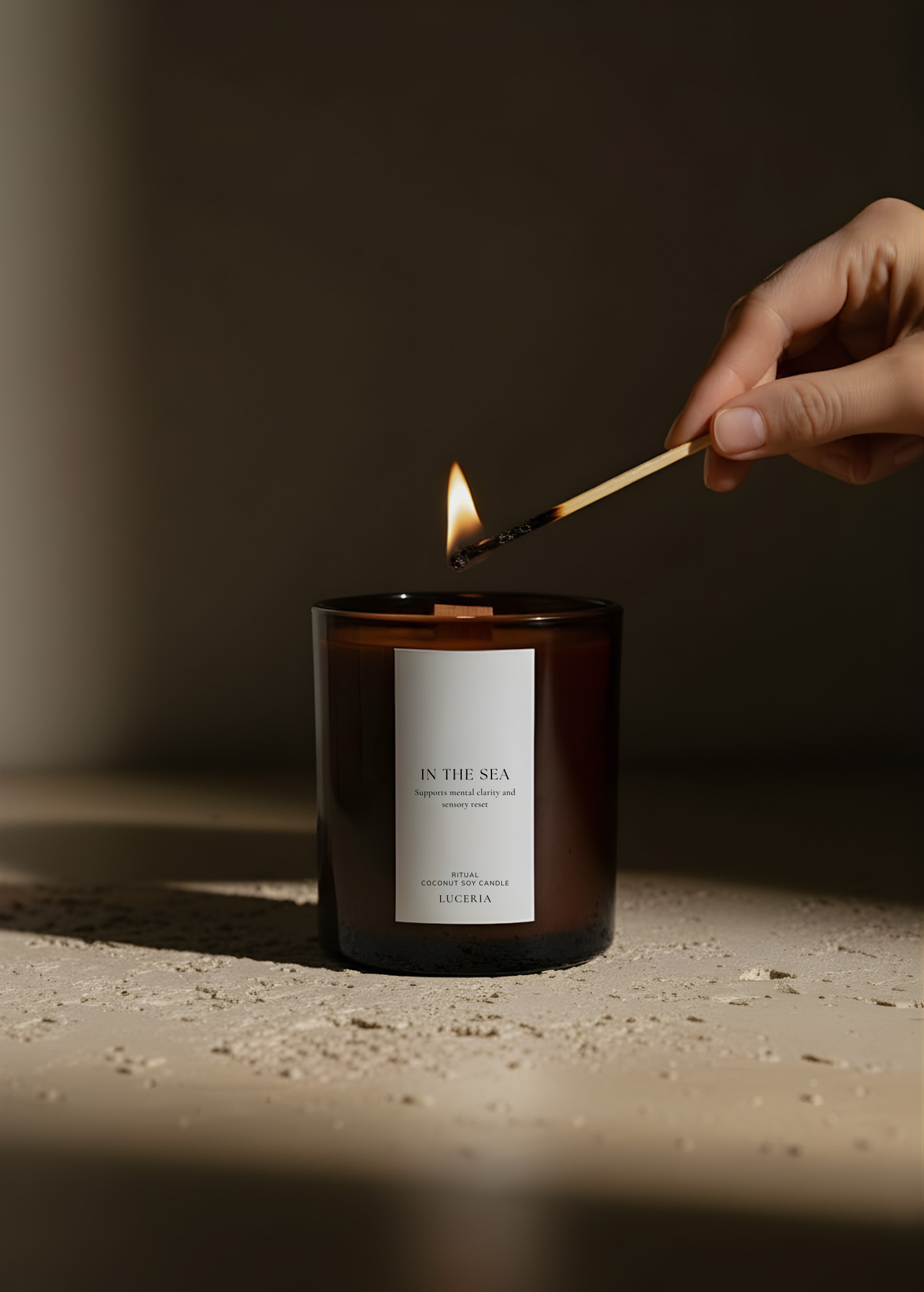 Hand lighting a candle labeled 'In the Sea' with a match against a dark background