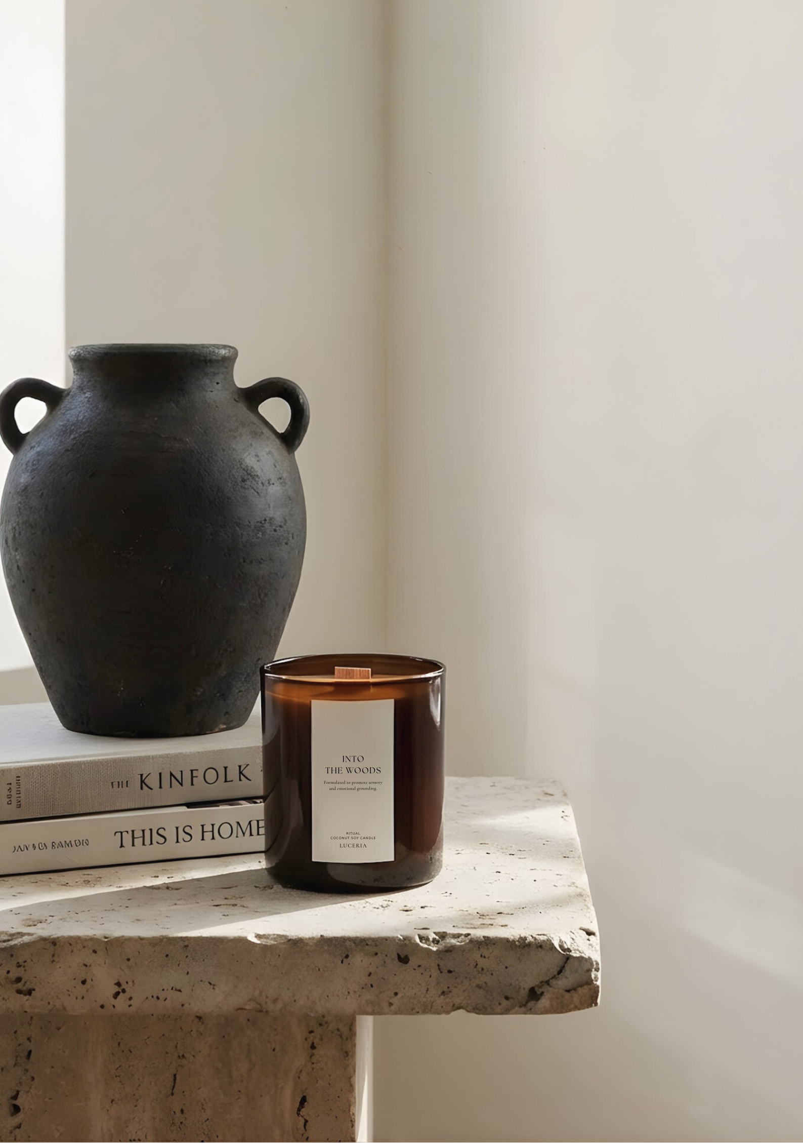 Black vase, books, and candle on a stone surface with a white wall background