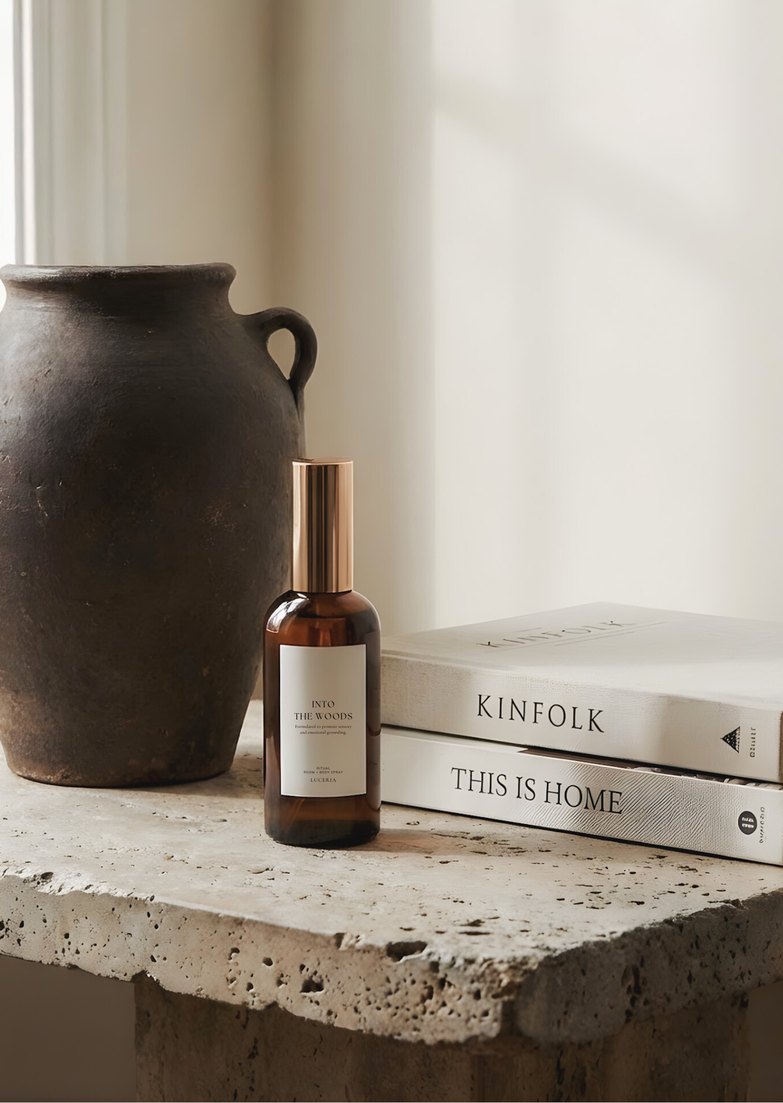A dark ceramic vase and a bottle on top of books titled 'KINFOLK' and 'THIS IS HOME' on a stone surface.