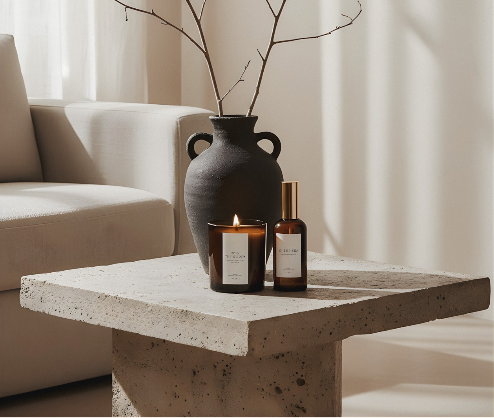Decorative setup with a vase, candles, and branches on a stone table in a softly lit room.
