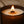 A close-up of a lit Luceria candle in a dark amber glass jar, with a single wick and a glowing flame. White text at the top reads, 'STRONG HOT THROW UP TO 90 HOURS BURN TIME.
