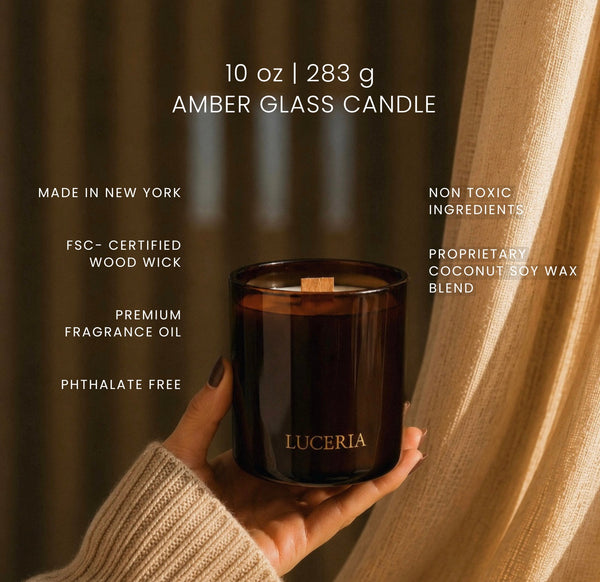 A hand holds a 10 oz amber glass candle by Luceria against a warm, draped beige curtain background. White text overlays highlight product features such as 'Made in New York', 'FSC-Certified Wood Wick', and 'Non Toxic Ingredients'.