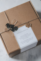 Gift box wrapped in brown box with a white label and eucalyptus leaf decoration on a light background