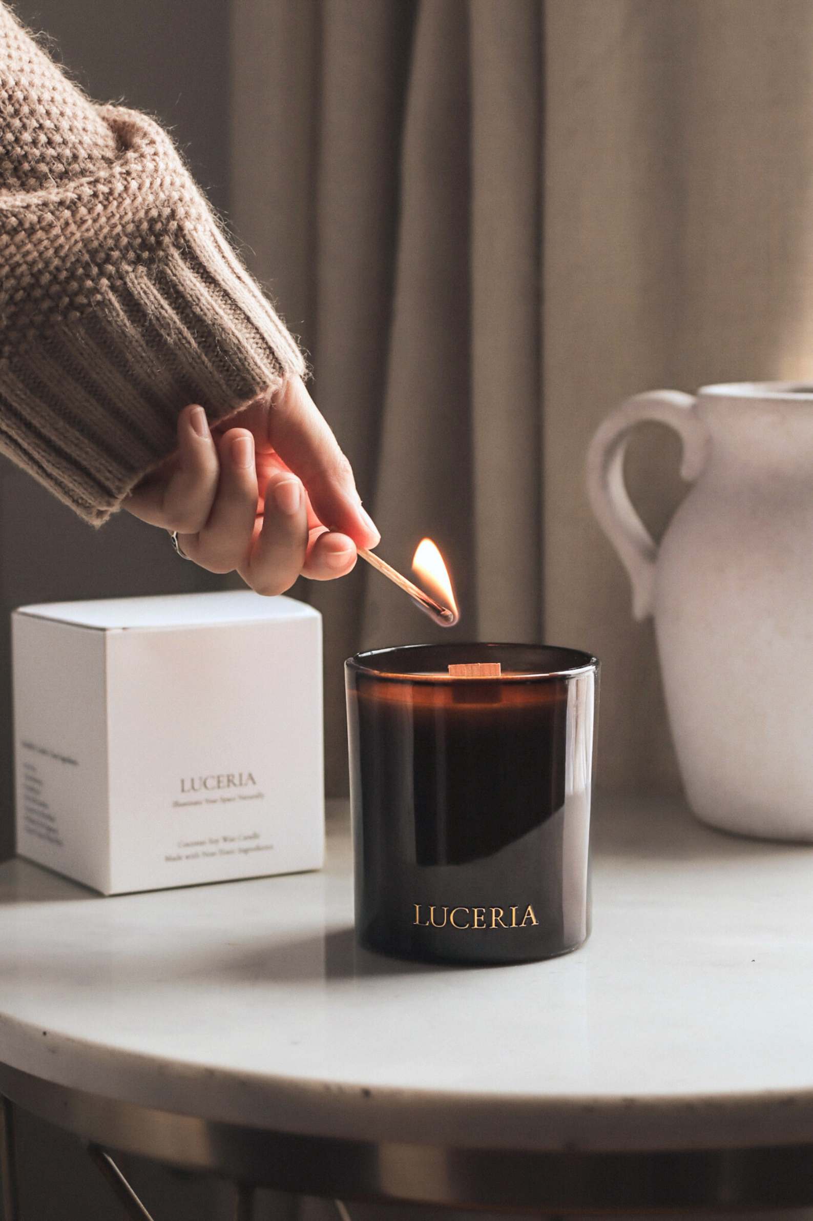 Person lighting a Luceria candle with a match on a table.