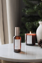 A bottle of rosemary and sage scented spray on a marble surface with a candle and decorative elements in the background.