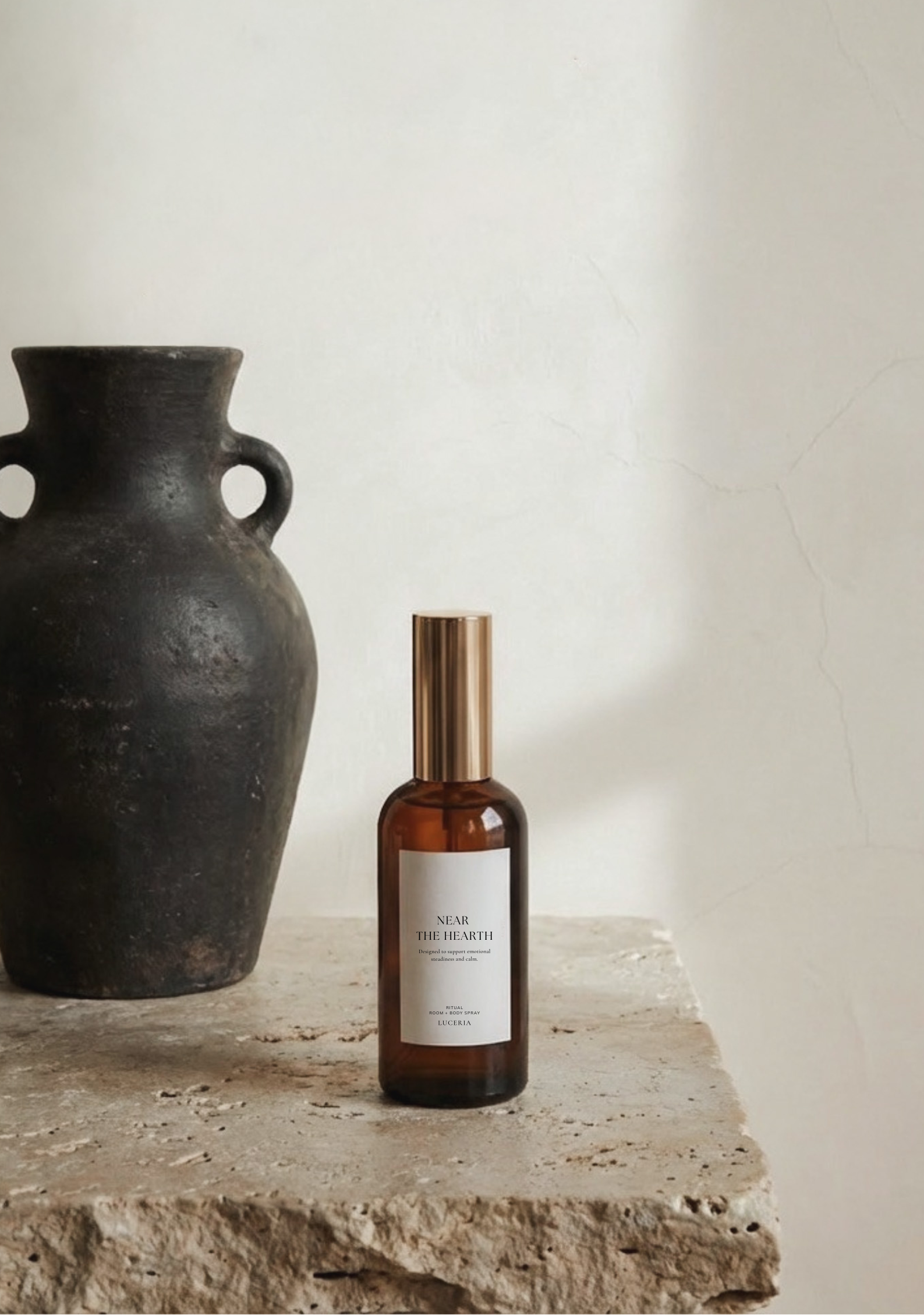 Brown bottle with gold cap on a stone surface next to a black vase against a white wall