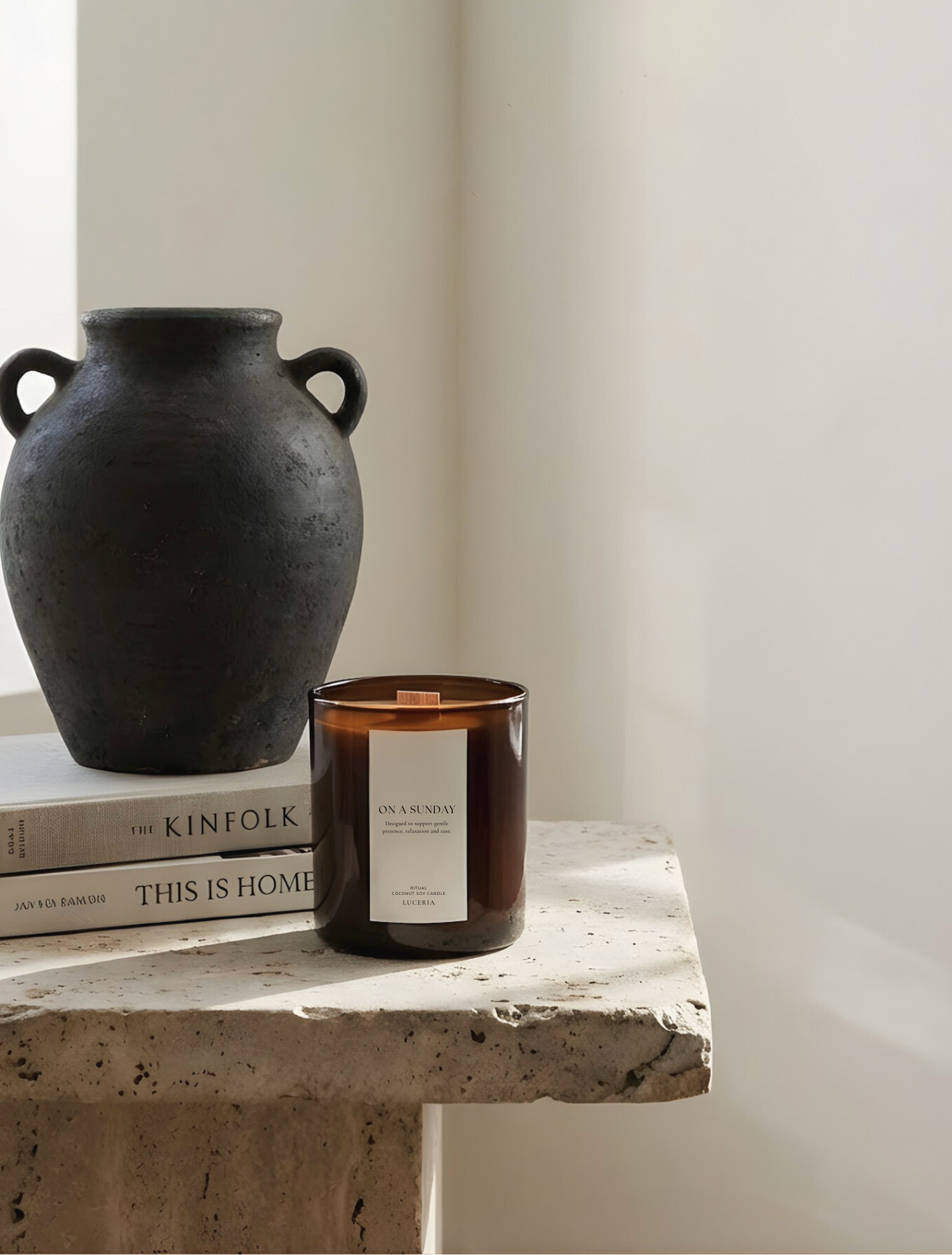 Black vase, books, and candle on a stone surface with a white wall background