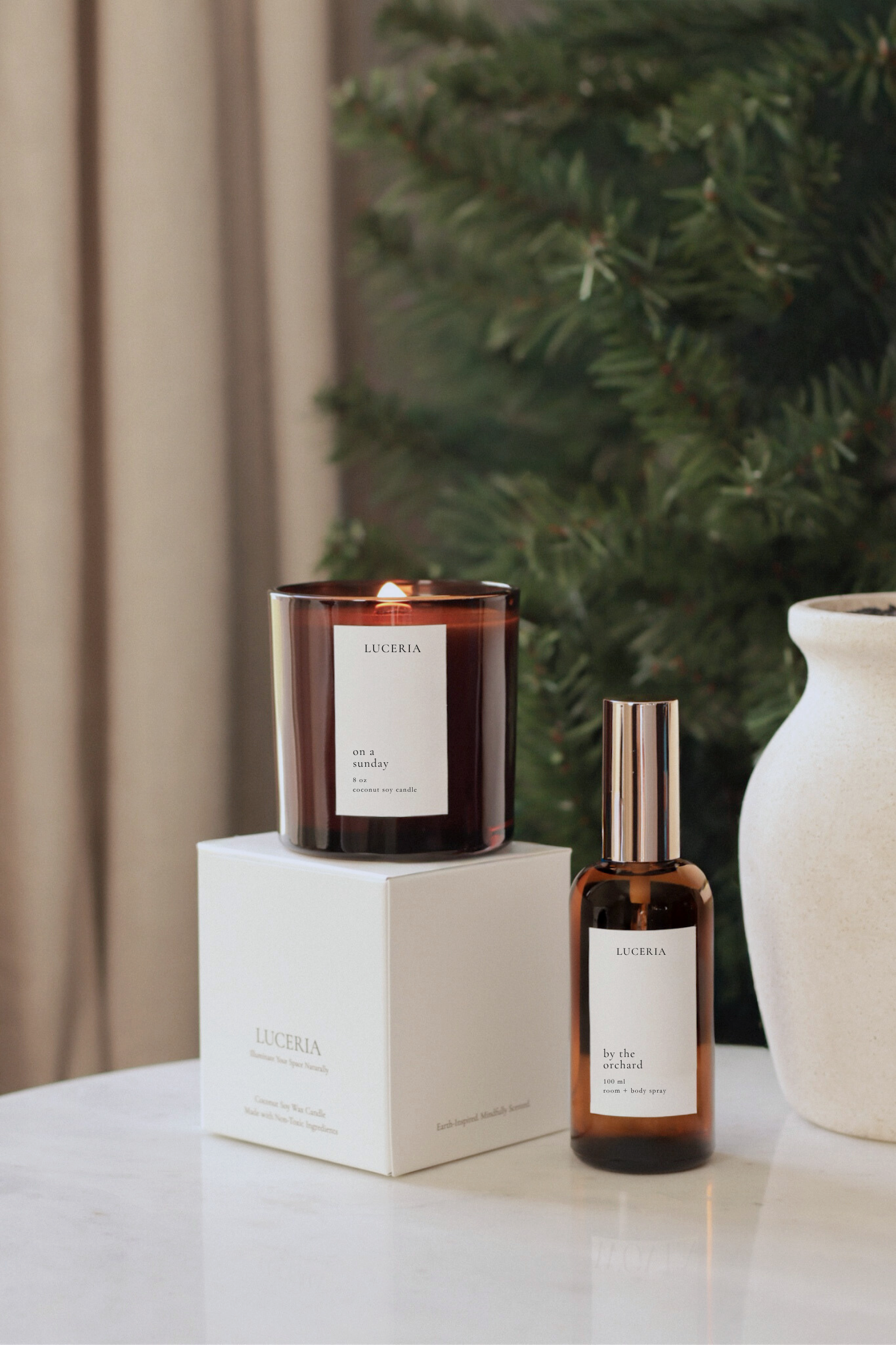Candle and bottle with labels on a white surface with a blurred green plant in the background