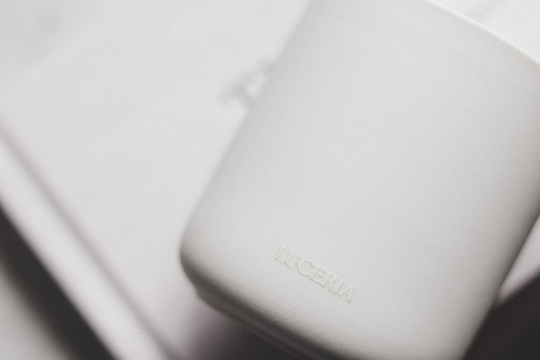 Close-up of a white ceramic candle with 'Luceria' branding on top of book background.
