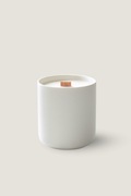 A minimalist white ceramic candle jar labeled 'LUCERIA' with a single wick on top, set against a solid light beige background. Luceria's Oakmoss and White Cedar Candle.